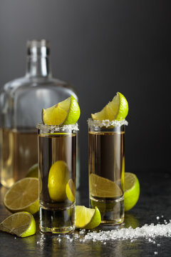 Tequila shots with salt and lime slices on a black stone table.