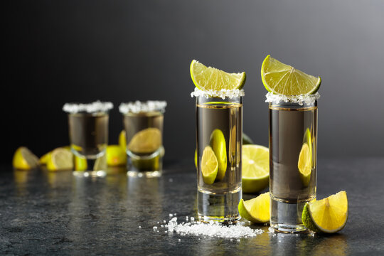 Tequila shots with salt and lime slices on a black stone table.