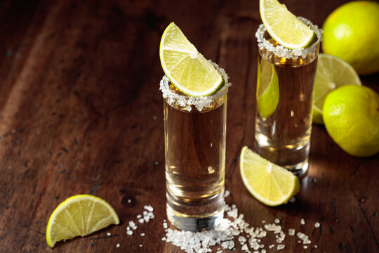 Tequila with salt and lime slices on an old wooden table.