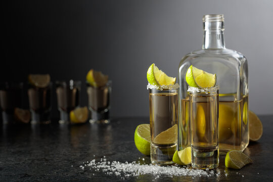 Tequila shots with salt and lime slices on a black stone table.