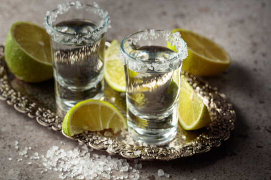 Tequila with salt and lime slices on a silver tray.