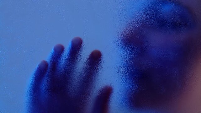 Anonymous woman touching wet matte glass with hand. Closeup of her face and fingers. Tenderness and loneliness concept. 