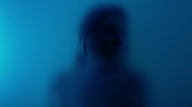 Abstract anonymous woman portrait behind the matte glass in blue light. Melancholy and femininity concept with copyspace 