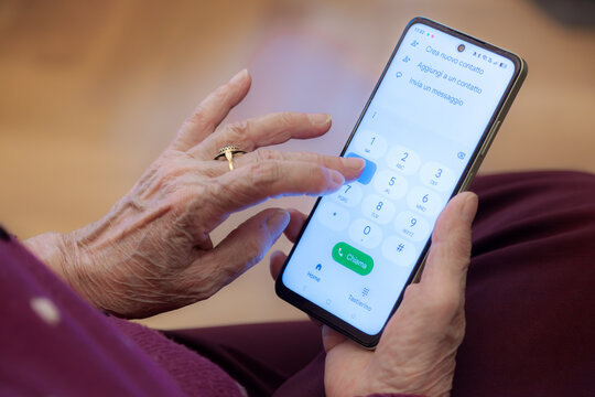 An elderly woman's hands hold a smartphone showing a dial pad, about to make a phone call, highlighting technology adoption and communication among seniors.