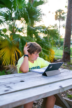 Boy doing homework outdoors with tablet and notebook