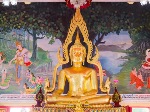 Golden seated Buddha statue in a temple interior with detailed religious murals painted on the wall behind it.