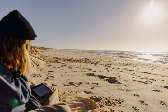 UGC Woman reading on sandy beach at autumn sunrise by the ocean