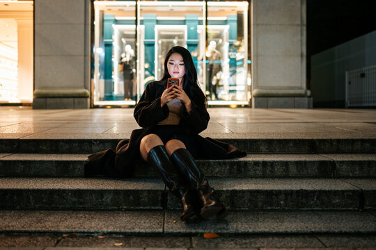 Woman sitting using smartphone in Tokyo at night