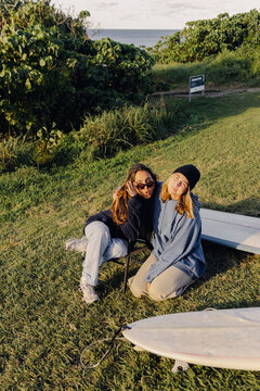 Two friends posing with surfboards on grassy coastal lookout in autumn