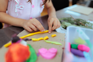 Naklejka premium Child Hands Rolling Yellow Clay Rollers On Craft Paper Board. Little girl fingers stretching vibrant plasticine cylinder making colorful artwork 