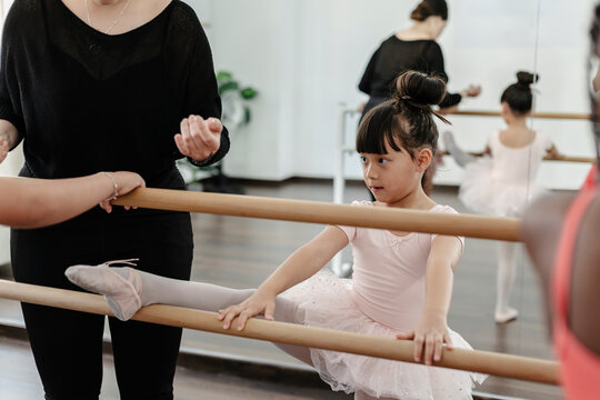 Young girl learning ballet stretching leg at barre