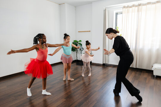 Ballet teacher guiding young diverse students practicing dance class