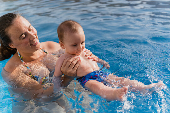 Mother teaching baby swimming in outdoor pool