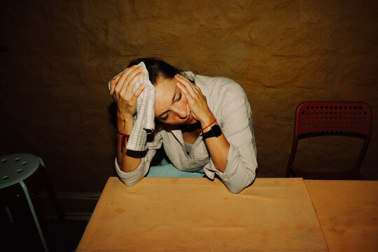 Tired Woman pressing a towel to her forehead at a Table