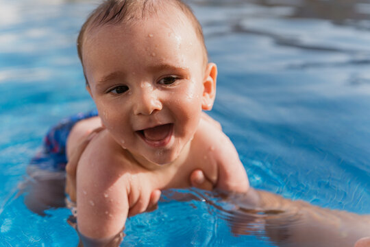 Happy baby enjoying first swimming lessons in pool