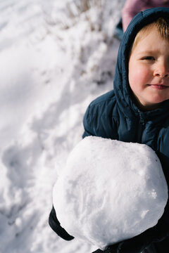 Boy holding large snowball on a snowy winter day