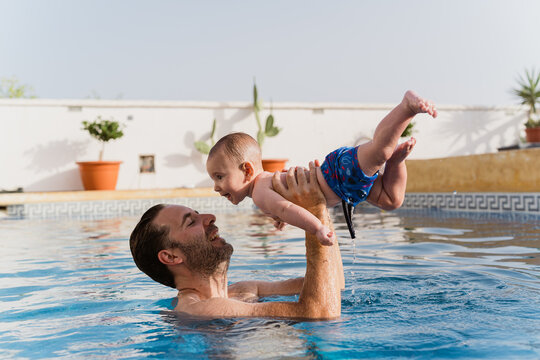 Father playing with baby in swimming pool during summer vacation