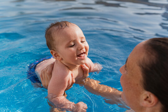 Mother holding happy baby learning swimming in pool