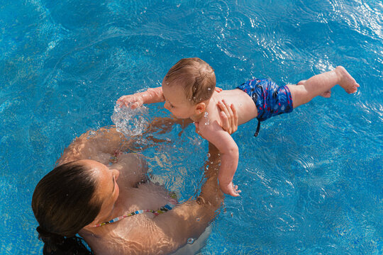 Mother teaching baby swimming in clear pool water