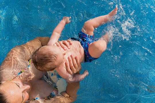 Mother teaching baby to swim in blue pool water