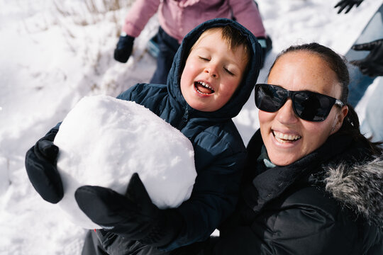 Mother and child creating large snowball enjoying winter playtime