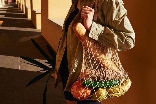Woman carries a mesh bag filled with fresh fruits and vegetables