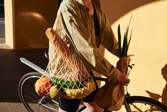 Woman with bicycle and net bag with fruits and baguette