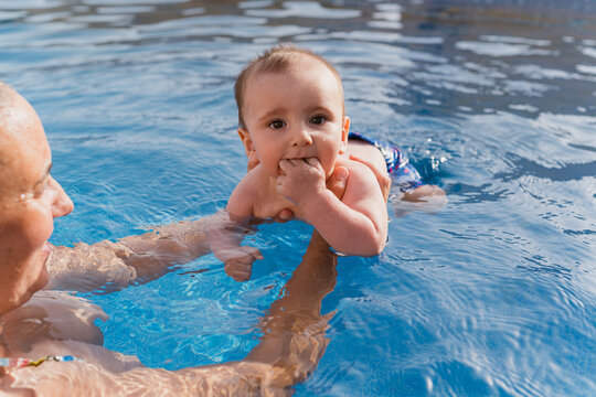 Parent teaching baby swimming in blue pool water