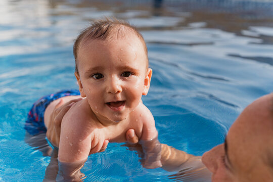 Happy baby splashing in pool water with father