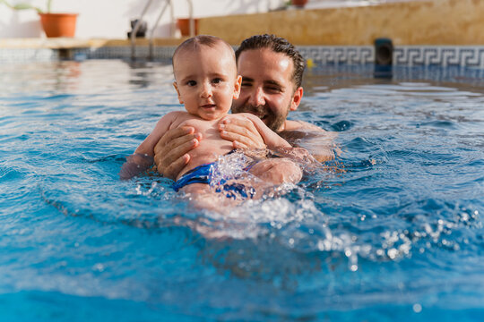 Father teaching baby swimming in pool water