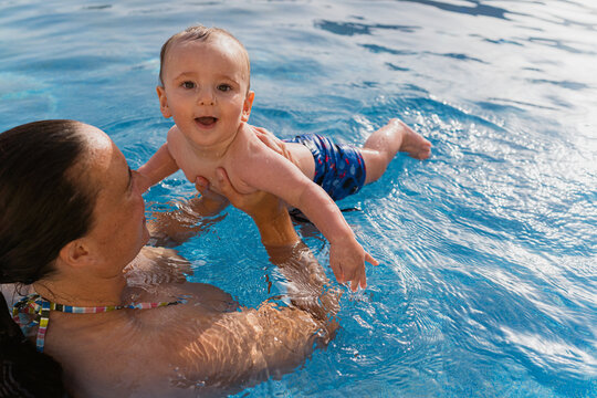 Mother teaching baby swimming in clear pool water