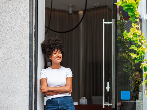 Smiling Female Small Business Owner Standing at Storefront Glass 