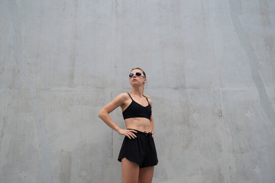 Sporty woman in black activewear standing near concrete wall