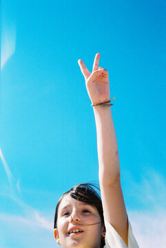 Child Raises Hand With Peace Sign Under Clear Blue Sky