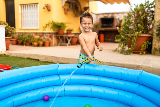 Happy toddler filling inflatable pool with water hose