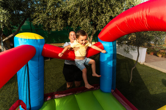 Mother helping child bounce on inflatable castle enjoying summer