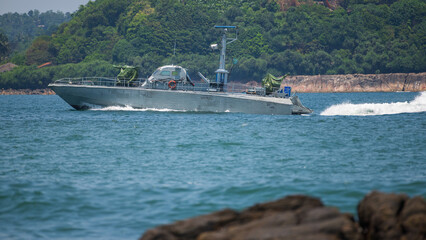 Obraz premium Naval patrol boat cruising through coastal waters on a sunny day against a lush green mountain backdrop