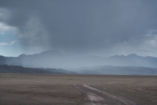 Dirt road leading toward mountains during a dramatic rain storm in a desert landscape. Commercial background for travel, adventure, and copy space.