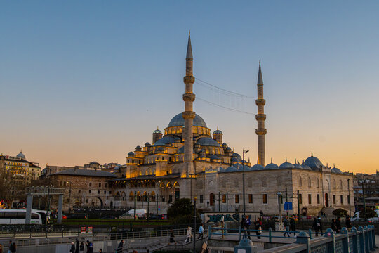 Illuminated New Mosque (Yeni Camii) at sunset, view from Galata Bridge in Istanbul, Turkey. Grand Ottoman architecture with dome and minarets at dusk