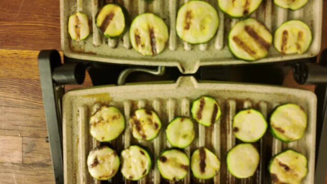 Close-up of zucchini slices grilling with distinct char marks on a griddle