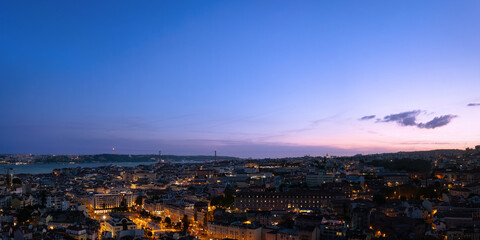 High angle panoramic view of Lisbon city skyline at dusk with illuminated streets, historic...