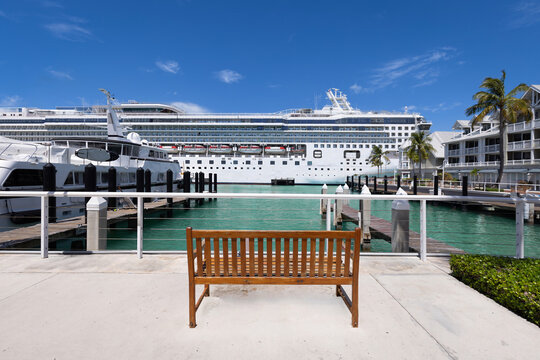 Empty wooden bench on a sunny waterfront promenade in Key West Florida with a large cruise ship docked in the turquoise harbor under a blue sky