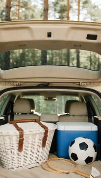 Open Car Trunk Packed With A Wicker Picnic Basket A Blue Cooler A Soccer Ball And Badminton Rackets For A Family Vacation Road Trip And Outdoor Leisure In A Green Forest