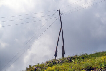 Fototapeta premium Utility pole on hill with wires against overcast sky