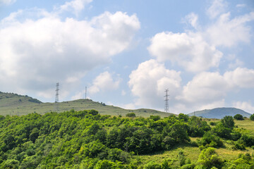 Obraz premium Green hillside with power line towers under cloudy sky