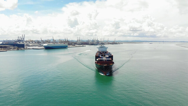 Large Oil tanker ship navigates through green ocean waters toward industrial port with prominent cranes under cloudy skies, showcasing global maritime transport and logistics solutions.