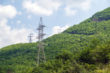 Obraz premium Green hills covered in trees with electricity pylons against a blue sky