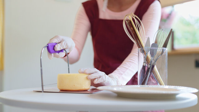 Asian woman cutting yellow cake with wire cutter while making homemade dessert in bright kitchen