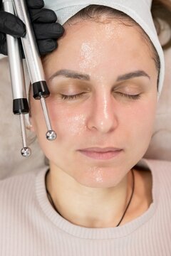 Microcurrent therapy. Face procedure. Professional woman cosmetologist hand using modern device for relaxing lifting massage in spa.