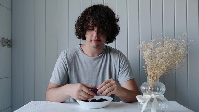 Young man enjoys food at table in a simple kitchen setting during daytime